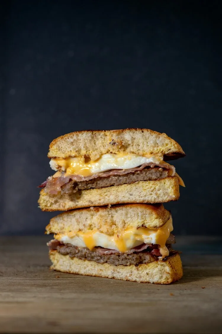 Two halves of an egg and cheese breakfast sandwich stacked on a wooden board