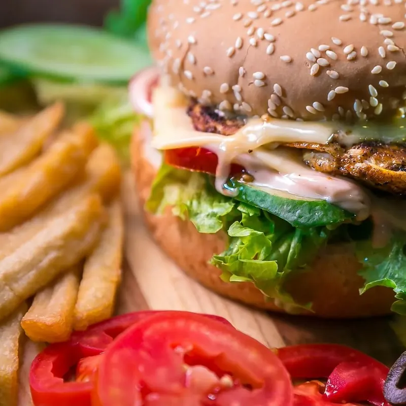 A sesame-bun burger with lettuce and melted cheese beside fries, sliced tomato and olives