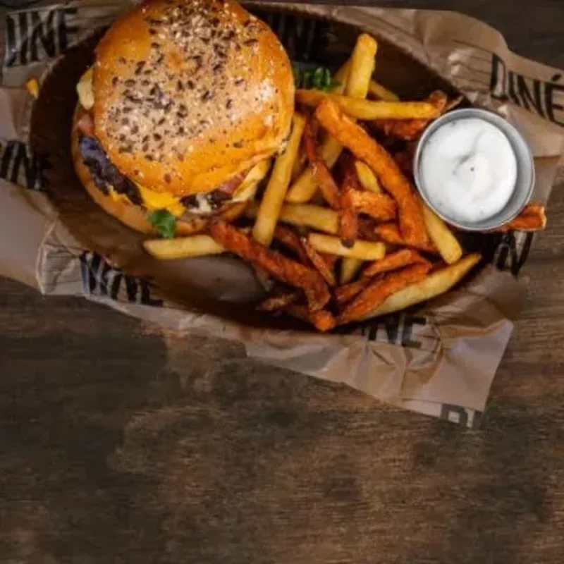A dark wood table with a burger basket, a grilled sandwich, a wrap and a salad at its edges
