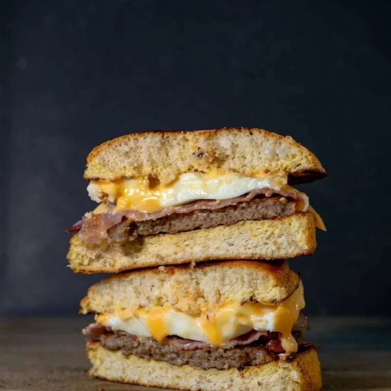 Two halves of an egg and cheese breakfast sandwich stacked on a wooden board